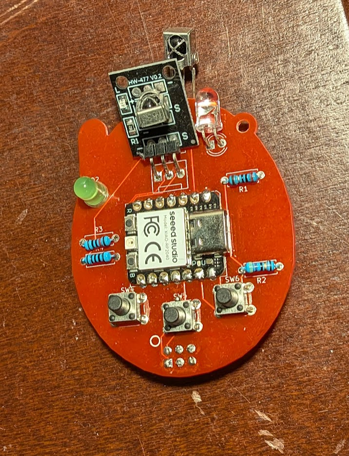 A red PCB in the shape of the outline of a Tamagotchi with buttons, a little seeed xiao rp2040, and IR receiver and transmitter soldered to it